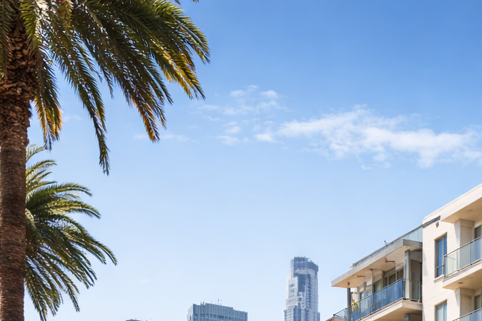 Edificio moderno de apartamentos en California con palmeras y skyline urbano al fondo