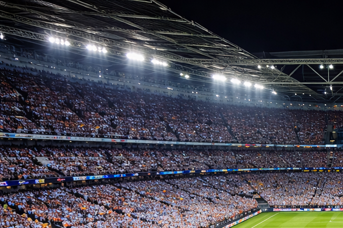 Estadio de fútbol lleno con aficionados y banderas gigantes de Argentina y España sobre el campo antes de un partido internacional.