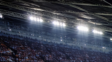 Estadio de fútbol lleno con aficionados y banderas gigantes de Argentina y España sobre el campo antes de un partido internacional.