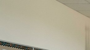 Aula pública en Texas con pizarrón, bandera de EE.UU. y un cartel religioso al fondo, sin que domine toda la imagen.
