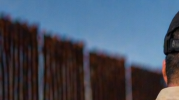 Oficial de seguridad deteniendo a un hombre cerca de la frontera en Texas junto a una patrulla y muro fronterizo.