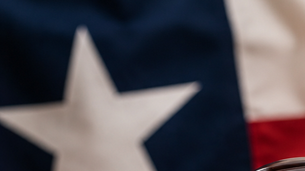Mazo de juez y balanza de la justicia con la bandera de Texas desenfocada al fondo, en referencia a la orden ejecutiva de Greg Abbott contra el llamado "birth tourism".