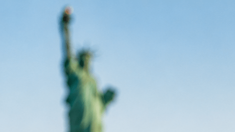 Green Card, pasaporte y bandera de Estados Unidos con la Estatua de la Libertad y el skyline de Nueva York al fondo.