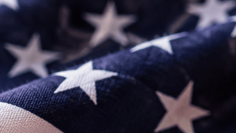 Documentos migratorios de Estados Unidos junto a un pasaporte, una bandera estadounidense y una tarjeta de residente, en una imagen sobre el aumento de tarifas de USCIS.